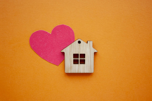 Love home, insurance and mortgage, marriage and valentine concept. Small wooden house toy and paper heart shape on orange background top view  - 写真・画像