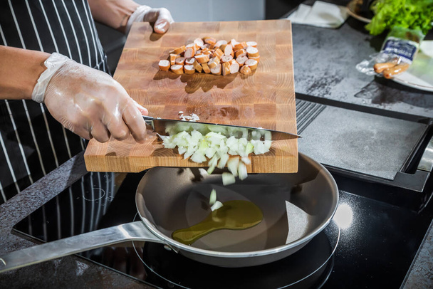 The cook transfers the chopped onion and sausages from the cutting board into a heated frying pan - Foto, Imagem