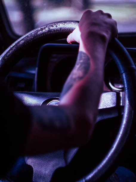 Primer plano de un hombre tatuado mano en un volante en un coche viejo en Europa, volante está a la izquierda
 - Foto, imagen