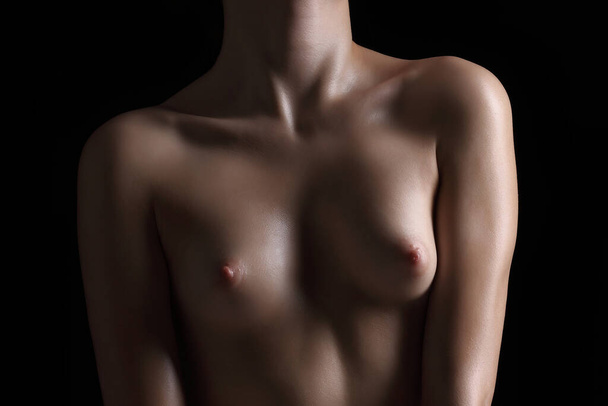 young female body with beautiful small breasts on a dark background - Fotografie, Obrázek