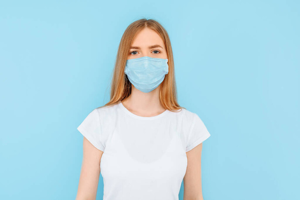 Protection from infectious diseases, coronavirus. A young girl wears a hygiene mask to prevent infection, airborne respiratory disease. closed Studio shot isolated on a blue background - 写真・画像