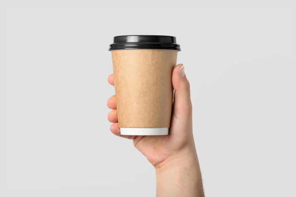 Mockup de mão masculina segurando um copo de papel de café isolado no fundo cinza claro.  - Foto, Imagem