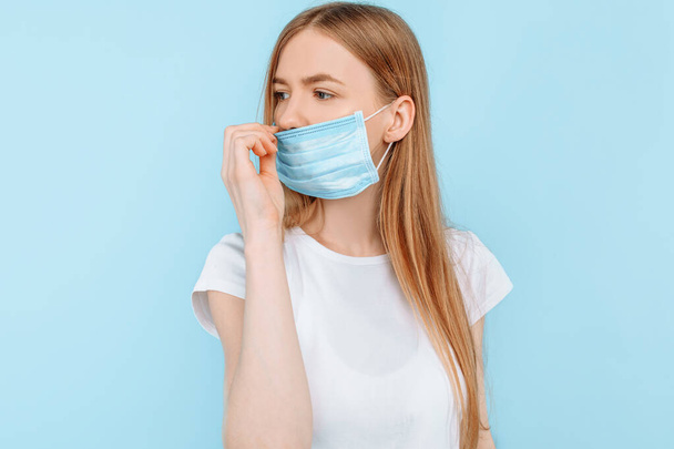 Protection from infectious diseases, coronavirus. A young girl wears a hygiene mask to prevent infection, airborne respiratory disease. closed Studio shot isolated on a blue background - Foto, imagen