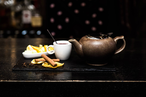 Mulled wine, sangria, mulled wine in a white Cup on a dark background, bar counter with fruit, tea and spices. Cinnamon sticks and orange - Foto, afbeelding