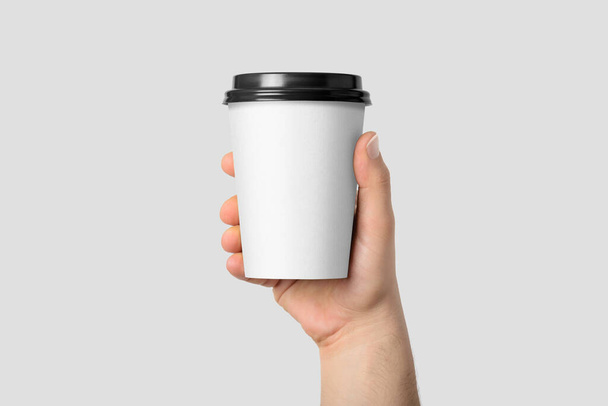 Attrappe einer männlichen Hand, die eine Kaffeepapiertasse auf hellgrauem Hintergrund hält.  - Foto, Bild
