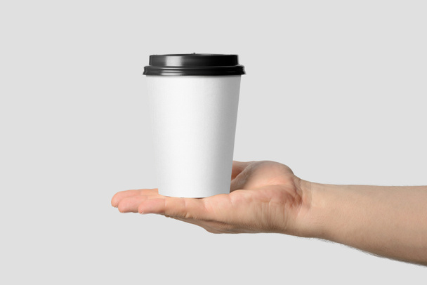 Макет чоловічої руки, що тримає чашку кавового паперу ізольовано на світло-сірому фоні
.  - Фото, зображення