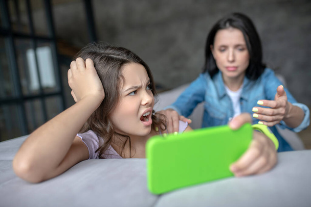 Mom and daughter having an agrument about using smartphone - Foto, afbeelding
