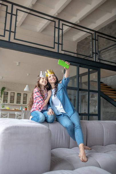 Mom and daughter wearing crowns and making selfie on a smartphone - Photo, Image