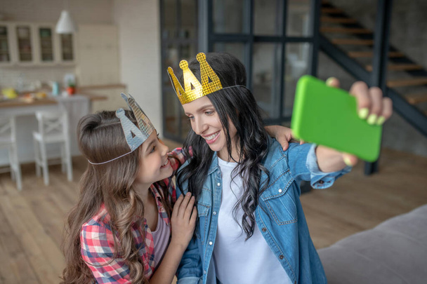 Mom and daughter wearing crowns and making selfie - Foto, afbeelding
