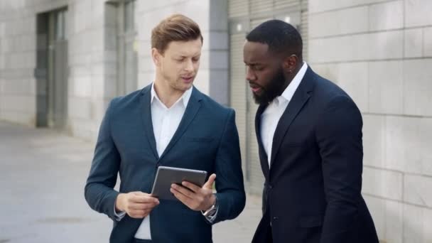 Businessmen using digital tablet on city. Male entrepreneurs talking outdoors - Footage, Video