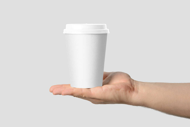 Attrappe einer männlichen Hand, die eine Kaffeepapiertasse auf hellgrauem Hintergrund hält.  - Foto, Bild