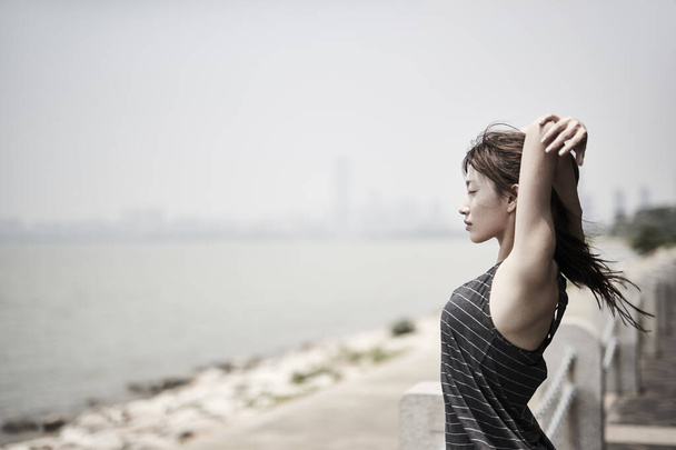 joven asiático adulto mujer estirando brazos al aire libre por el mar, vista lateral
 - Foto, Imagen