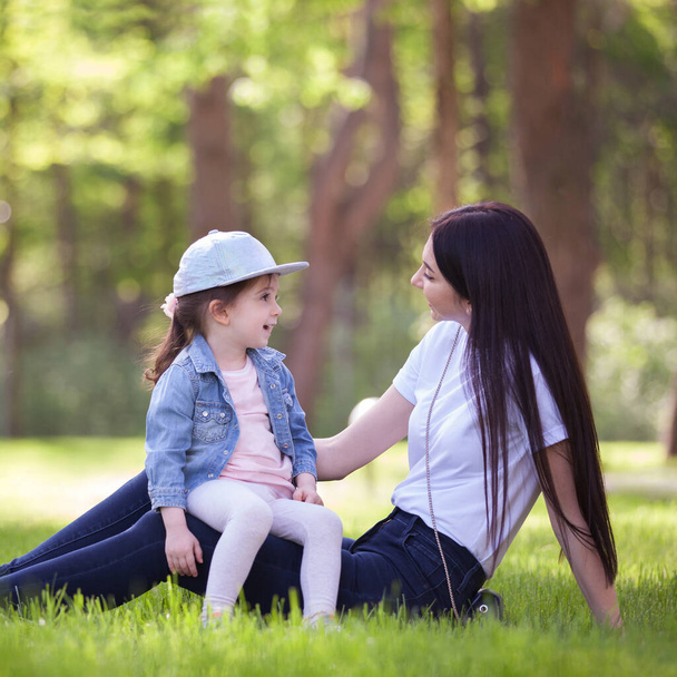 Happy mother and daughter relaxing in the park. Beauty nature scene with family outdoor lifestyle at spring or summer time. Happy stylish family resting together, having fun outdoor. - Foto, Imagen