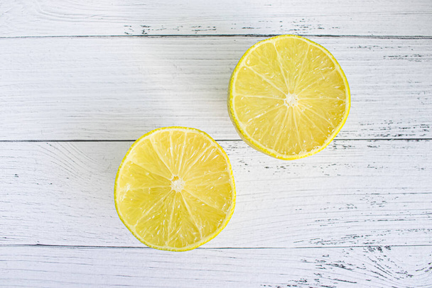 Two halves of yellow fresh lemon against the background of white wooden boards. Cut lemon on a white wooden table top view - Foto, Imagen