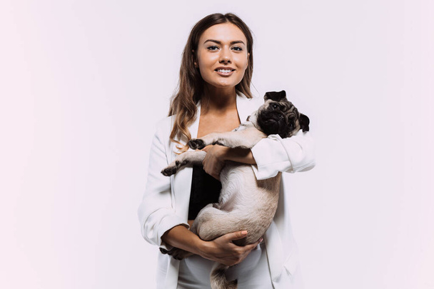 A laughing and smiling auburn haired woman in a white dress, is staring most lovingly at her cute pug, who calmly sits on the hands, gaining her undivided attention. Isolated white background - Photo, image