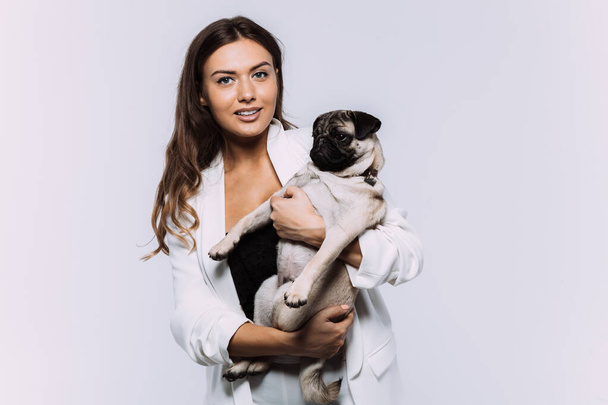 A laughing and smiling auburn haired woman in a white dress, is staring most lovingly at her cute pug, who calmly sits on the hands, gaining her undivided attention. Isolated white background - Fotó, kép