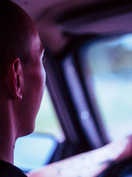 Rückansicht eines jungen tätowierten Mannes, der am Steuer sitzt und altes Auto fährt - Foto, Bild
