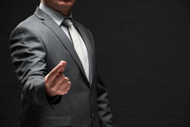 businessman demonstrating something in his fingers, dressed in gray suit, dark wall background - 写真・画像