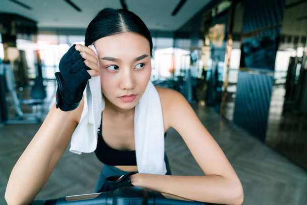 strong and firm asian woman sport wear relax on bicycle hand hold white napkin fitness background - 写真・画像
