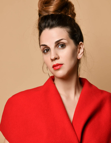 Brunette girl with evening make-up, in earrings and red shawl. She is posing standing against beige studio background. Close-up - Φωτογραφία, εικόνα