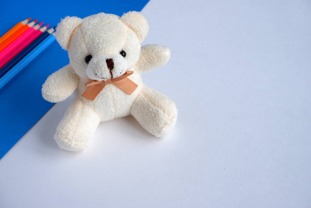 Beautiful beige Teddy bear, colored pencils on a blue and white background. Soft toy. School supplies.  Suitable for advertising backgrounds and greeting cards - Φωτογραφία, εικόνα