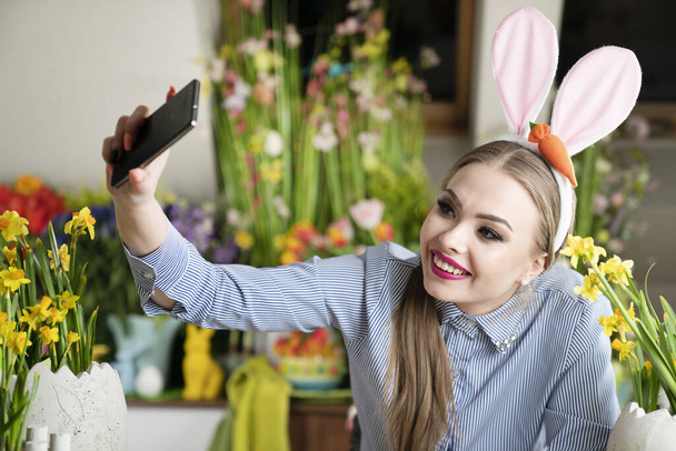 Cute young women with bunny ears painting easter eggs.  Easter background. Bouquets of spring flowers. Easter eggs in baskets. - Фото, изображение