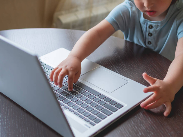 Child explores silver metal laptop. Curious toddler boy presses buttons. - Foto, afbeelding