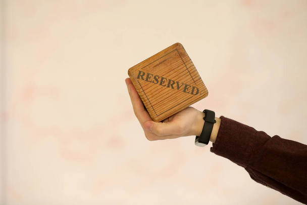 A wooden plaque has a word reserved . male hand holds a wooden plate with the inscription reserved isolated on a white background. selective focus. - 写真・画像