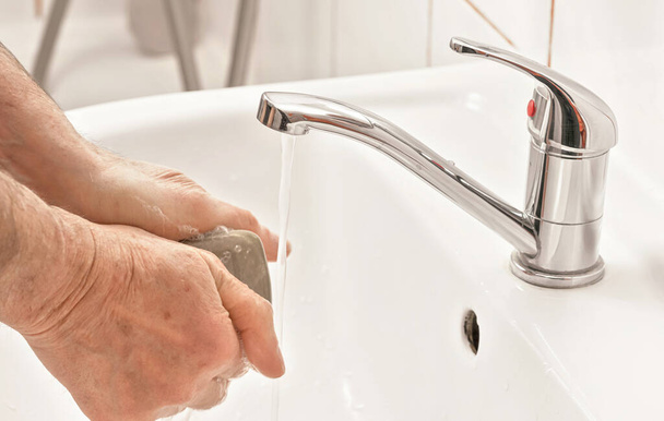 Senior man washing hands with soap under tap water faucet, closeup detail. Can be used as hygiene or prevention concept during ncov coronavirus / covid 19 outbreak - Photo, Image