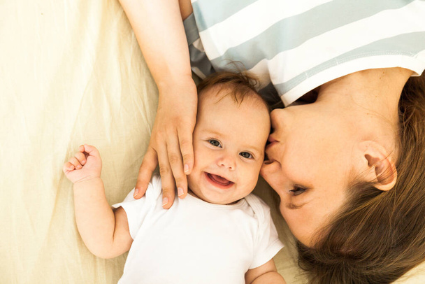 Vista superior de una madre feliz besando a un bebé acostado en una cama
. - Foto, Imagen