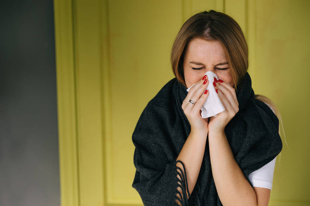 Mujer enferma vistiendo bufanda, sonándose la nariz y estornudando en el tejido. hembra tiene gripe, virus o alergia respiratoria. Concepto de salud, medicina y personas. Dolor de cabeza y fiebre remedios. - Foto, Imagen