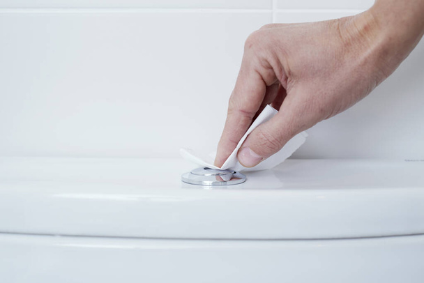 крупним планом білий чоловік натискає кнопку змиву туалету, покриваючи пальцями шматок туалетного паперу
 - Фото, зображення
