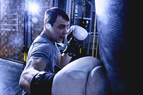 boxeur professionnel homme musclé bat sac de boxe dans des gants de boxe, l'entraînement d'un athlète dans la salle de gym, la bataille agressive dans des couleurs sombres, portrait en gros plan
 - Photo, image