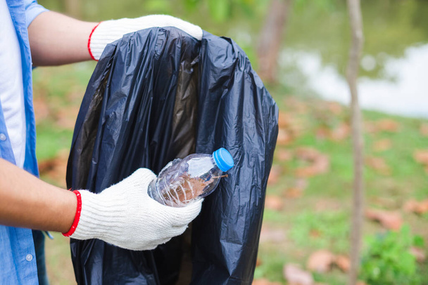 Lähikuva käsi nuoret vapaaehtoiset mies pitää pullo muovi laittaa jätesäkkeihin puhdistusalue puistossa, Vähennä muovia, vähentää ilmaston lämpenemistä
. - Valokuva, kuva