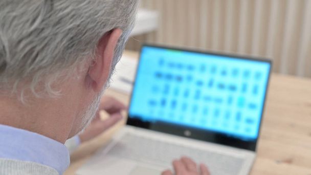 Vista trasera del anciano mayor que trabaja en el ordenador portátil, desplazamiento
 - Foto, imagen