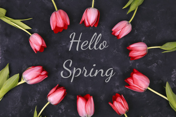 Hello spring text sign. Stylish pink tulips on black rustic background top view. Flat lay. - Photo, image