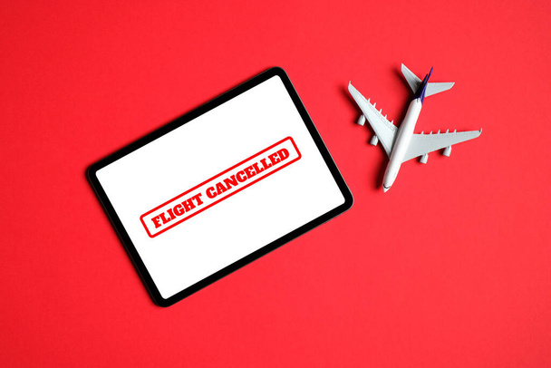 Flight cancelled concept. Plane model and tablet with stamp "Flight cancelled" on the screen over red background. Top view, flat lay. - Photo, Image