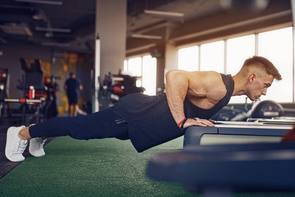 Young athletic man doing push-ups in gym. Muscular and strong guy exercising. - Foto, Imagem