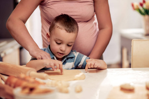 妊娠中の母親と彼女の息子は台所で楽しみ、クッキーを作る. - 写真・画像