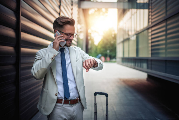Νεαρός επιχειρηματίας μιλάει στο τηλέφωνο μπροστά από ένα κτίριο γραφείων. - Φωτογραφία, εικόνα