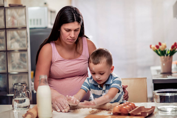 Έγκυος μητέρα και ο γιος της απολαμβάνουν στην κουζίνα και να κάνει τα μπισκότα. - Φωτογραφία, εικόνα