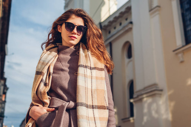 Street female fashion. Portrait of stylish young woman walking in city wearing coat sunglasses scarf on street outdoors. Spring accessories - Фото, зображення