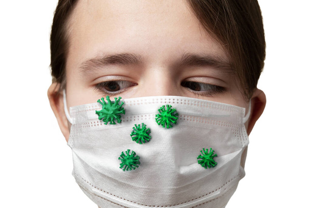 Koronaviry nebo jiné infekční mikrobi zelené barvy sedí na lékařské masce, nasazené na obličeji mladé dívky izolované na bílém. Koncepce ochrany před viry pomocí lékařské masky. - Fotografie, Obrázek