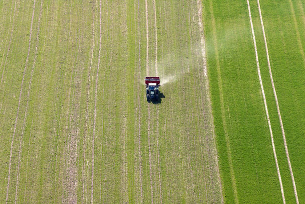 Farmář jezdí se svým buldokem přes pole a sype hnojivo - Fotografie, Obrázek