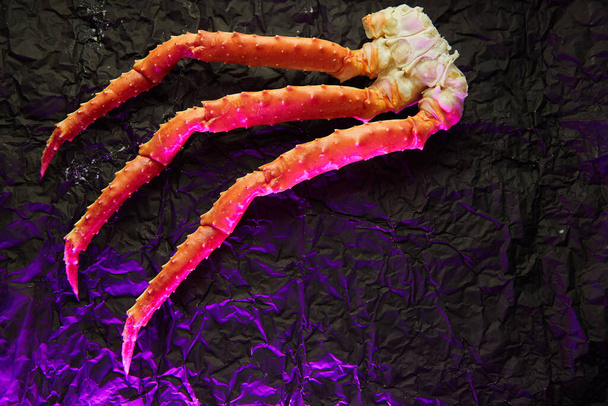 Imagen de falanges frescas de cangrejo sobre fondo oscuro en luz rosa con copyspace
 - Foto, Imagen