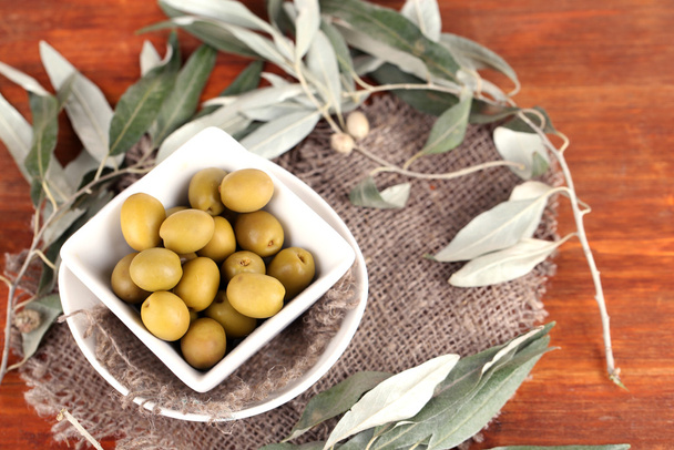 Olives in bowl with branch on sackcloth on wooden table - Photo, image