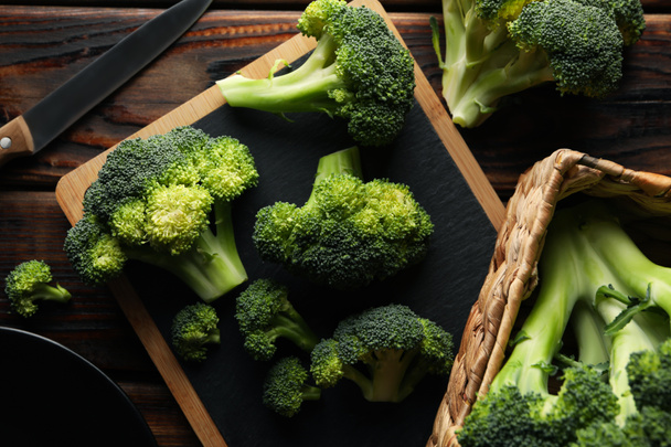 Board and basket with broccoli on wooden background, top view - Foto, afbeelding