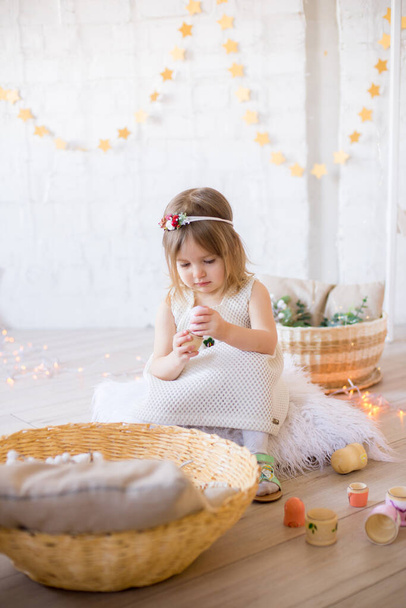 Little cute girl in a white dress plays in a bright children's room, decorated with toys and garlands. - Valokuva, kuva