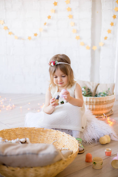 Beyaz elbiseli küçük tatlı kız oyuncaklar ve çelenklerle süslenmiş parlak bir çocuk odasında oynuyor.. - Fotoğraf, Görsel
