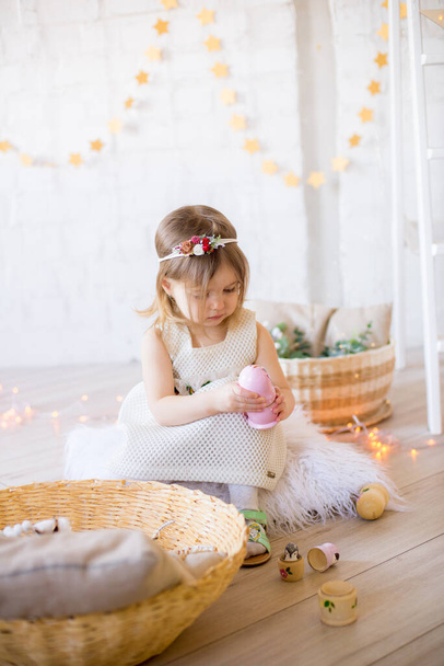 Little cute girl in a white dress plays in a bright children's room, decorated with toys and garlands. - Foto, imagen